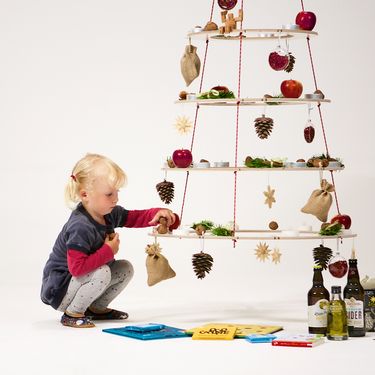 Ein Kind schmückt den nachhaltigen Weihnachtsbaum Josef mit Nüssen, Äpfeln und Tannenzapfen